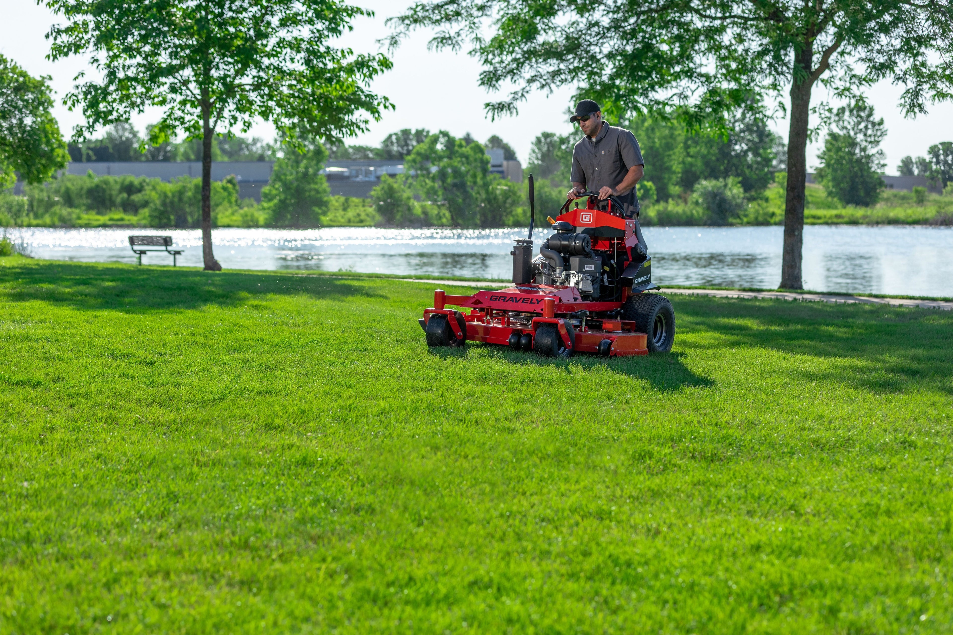 Person operating a red riding lawn mower on a grassy area near a body of water.